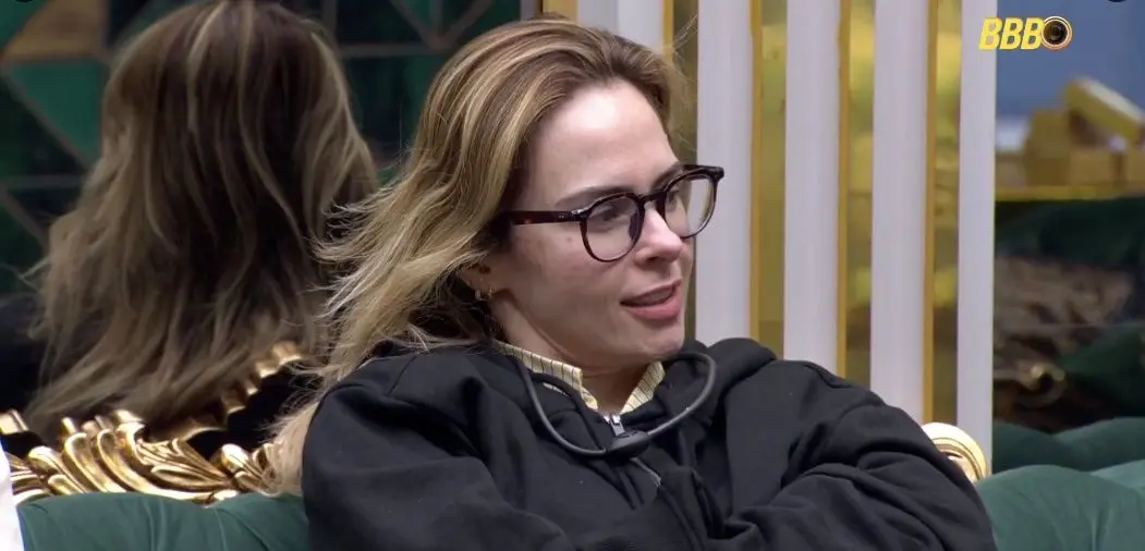 Imagem mostra a BBB Ana Paula, de óculos e sentada no sofá da sala do realty.