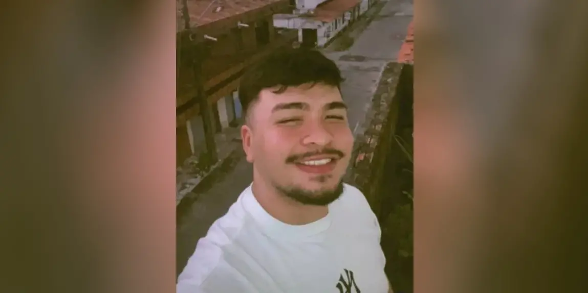 Rosto de jovem de cabeços pretos, que sorri para foto e usa camiseta branca.