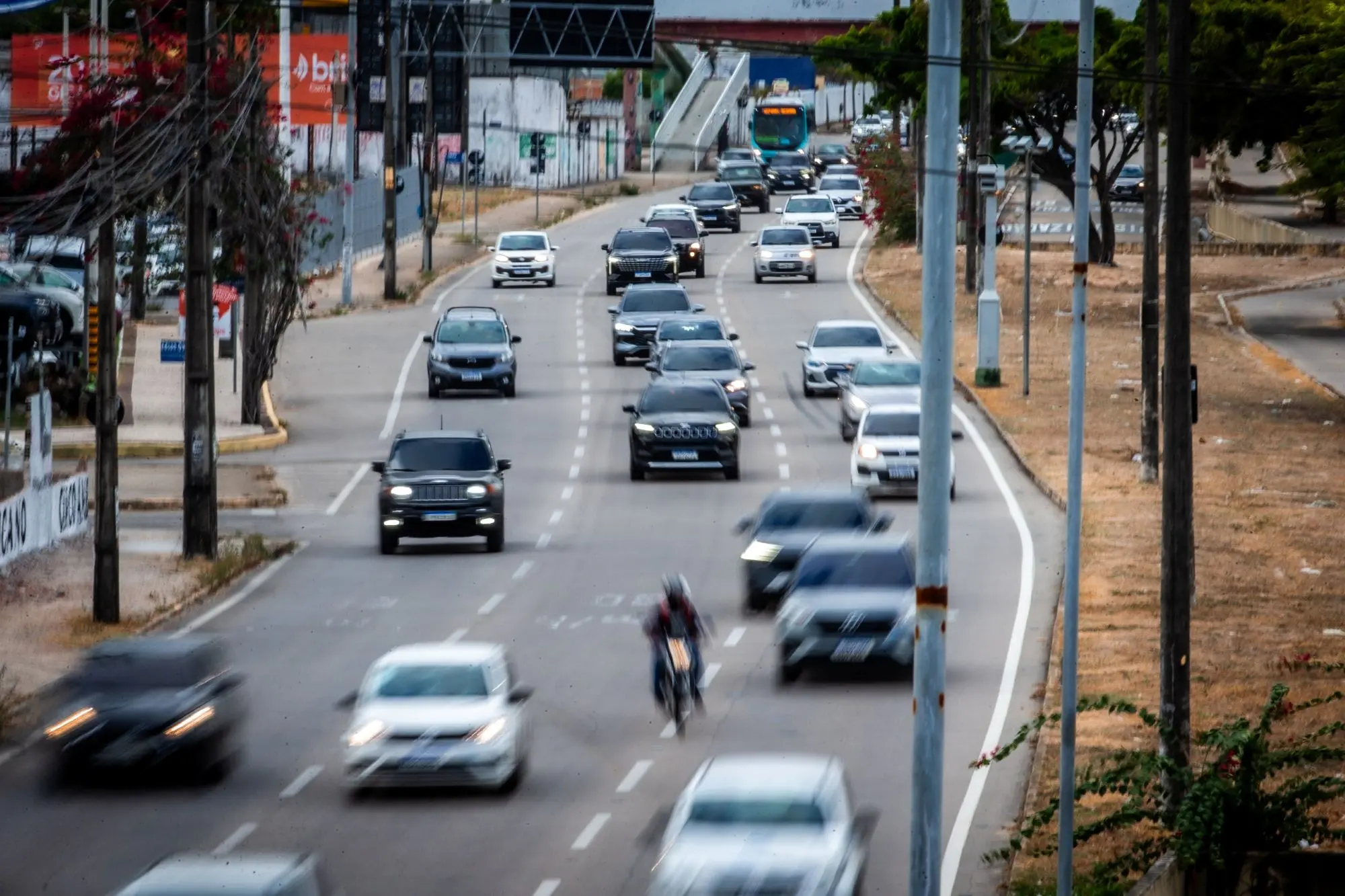 Avenida movimentada com múltiplos carros em trânsito e um ciclista em uma das faixas.