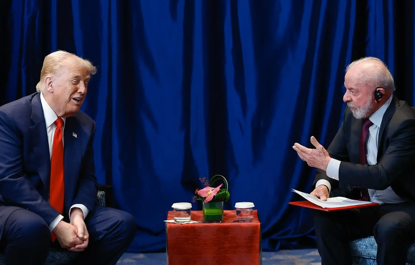 Lula e Trump conversam pessoalmente em frente a uma cortina azul.