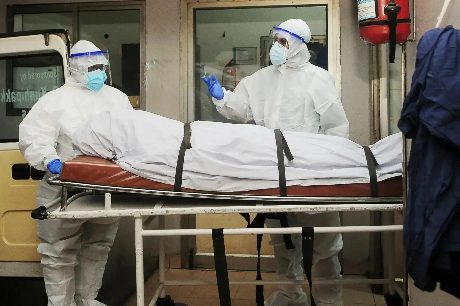 Dois profissionais de saúde usando equipamentos de proteção individual transferindo o corpo de uma pessoa que morreu de infecção pelo vírus Nipah em um hospital particular da índia.