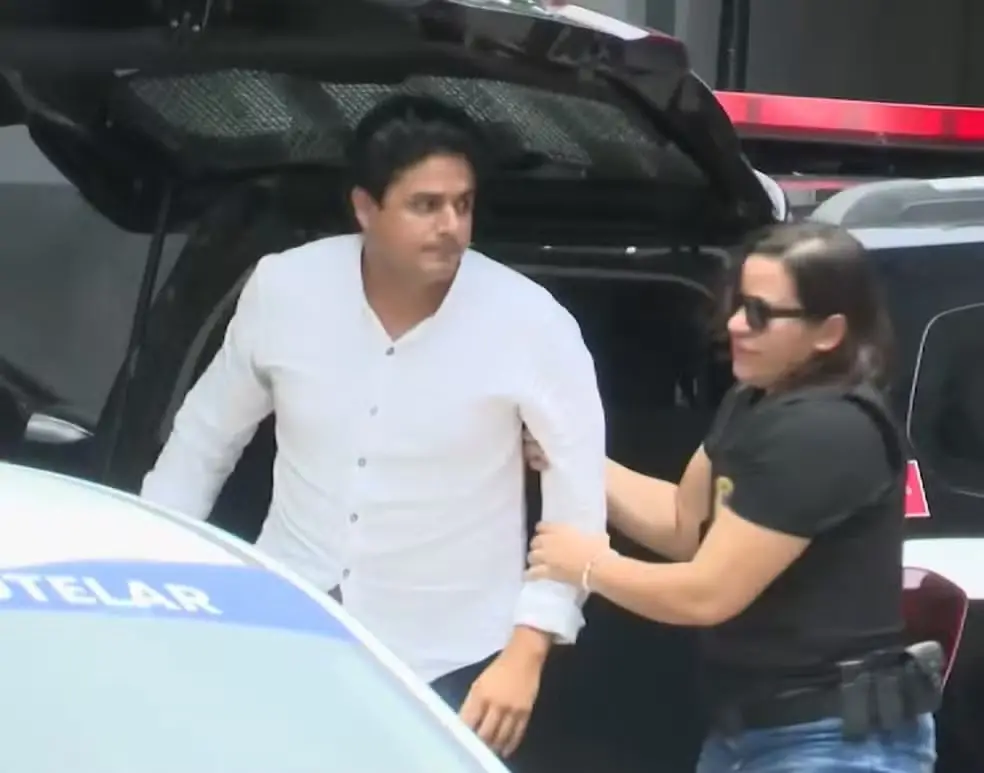 João Lima saindo de dentro da viatura e sendo direcionado ao presídio.