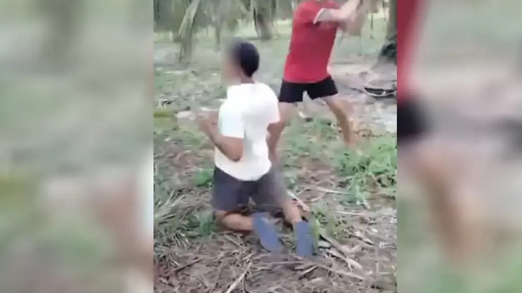 Homem sendo agredido por um adulto ao ar livre, situação de violência infantil ocorrendo em ambiente externo com vegetação ao fundo.