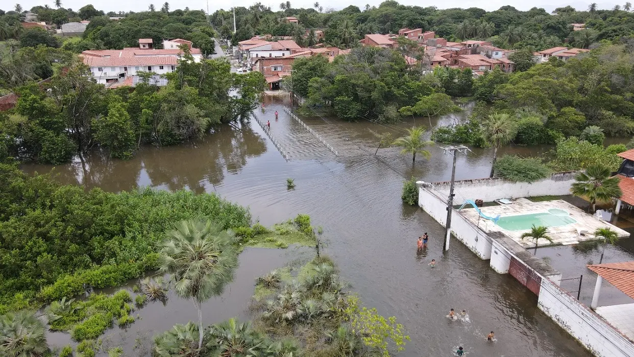Vista aérea do bairro Sabiaguaba mostra uma ponte totalmente coberta por alagamento. Acima da água, há árvores e algumas residências.