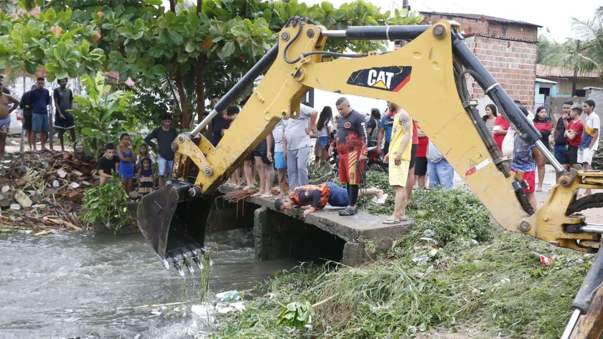 Foto de populares auxiliando na busca de adolescente desaparecido após ser arrastado em canal de Fortaleza.