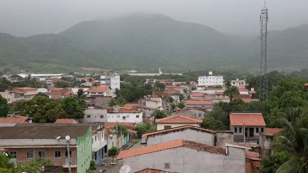 Vista aérea de Itapipoca, no Ceará, com colina com névoa ao fundo e, abaixo, casas simples.