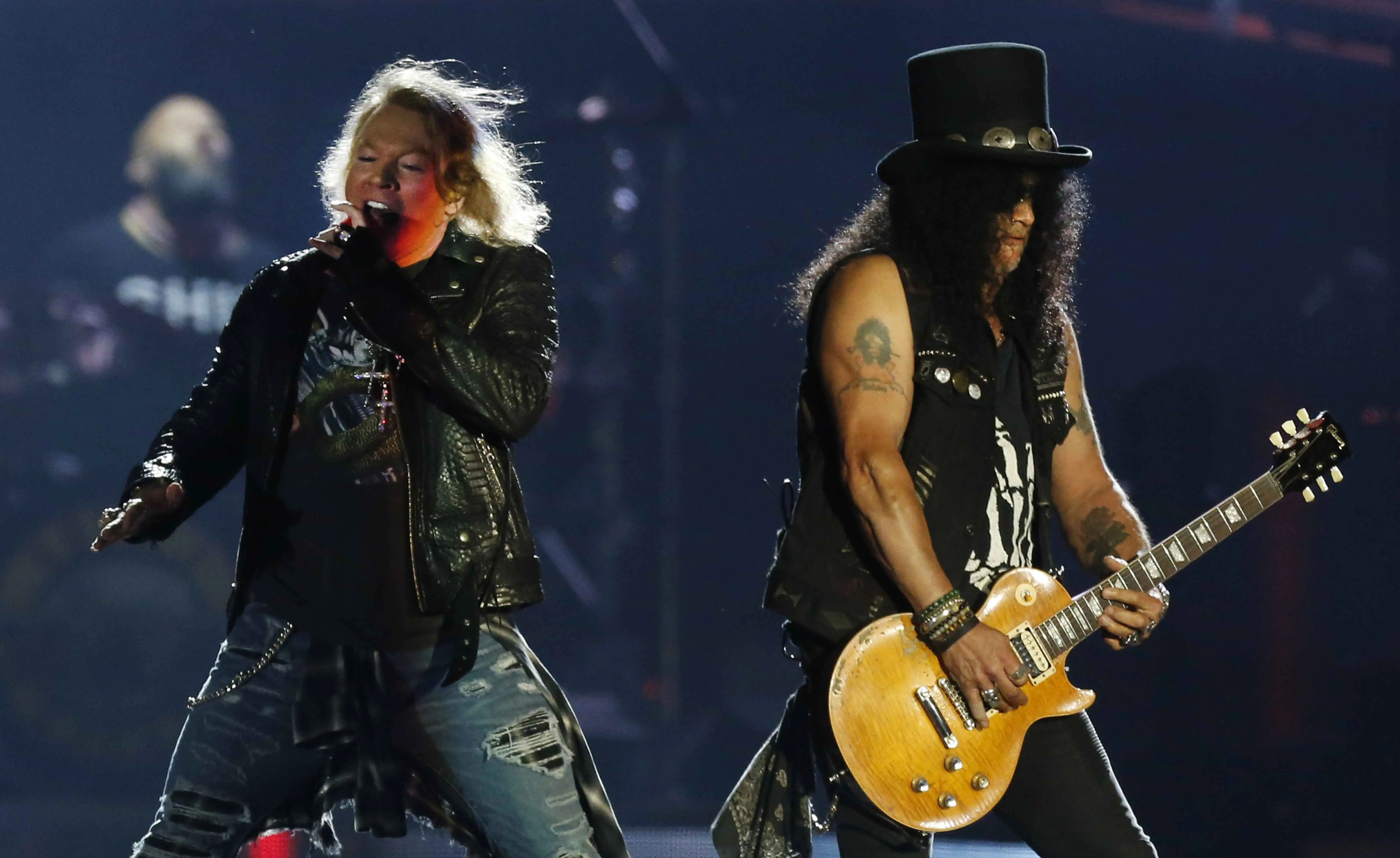 Imagem mostra Axl Rose cantando com um microfone enquanto Slash toca guitarra em um palco durante um show de rock do Guns N' Roses no Rio de Janeiro.