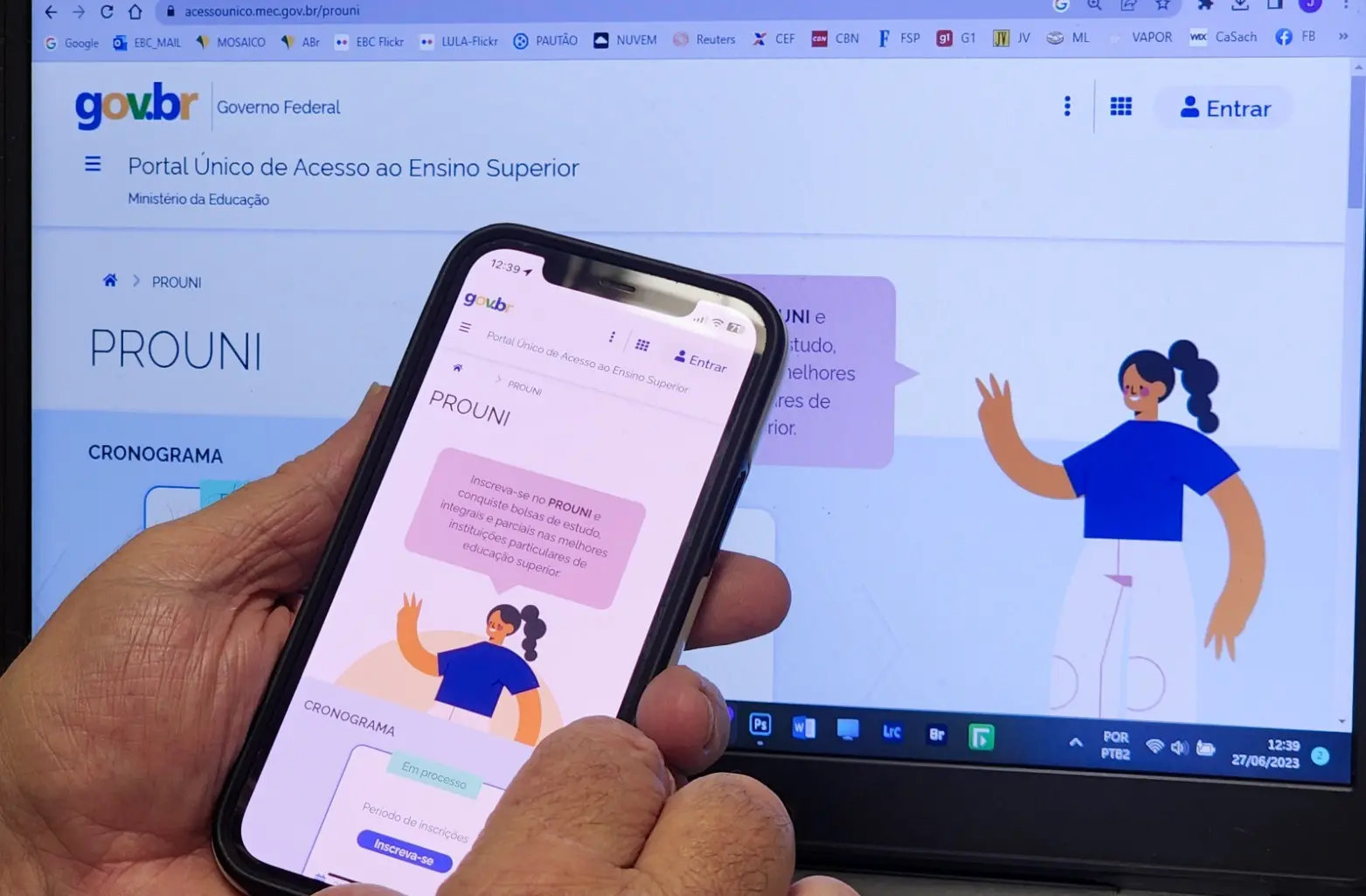 Mão segura celular em frente a um notebook aberto na tela inicial do Prouni.