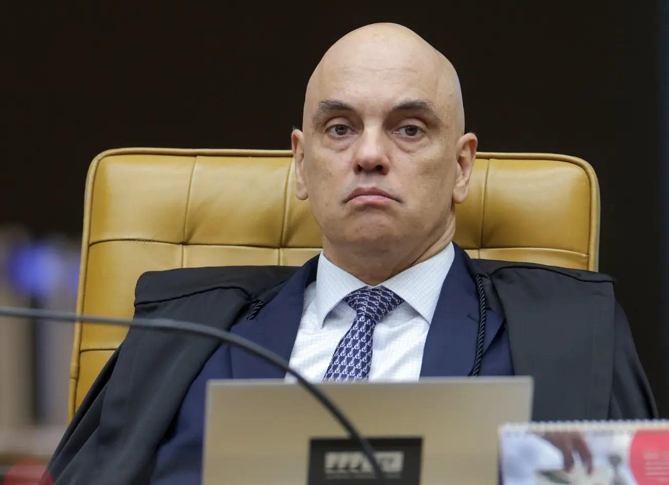 Alexandre de Moraes é um homem de meia idade, branco e careca. Na foto, ele está com expressão séria, no plenário do STF, e usa terno preto com camisa social branca e gravata estampada azul.