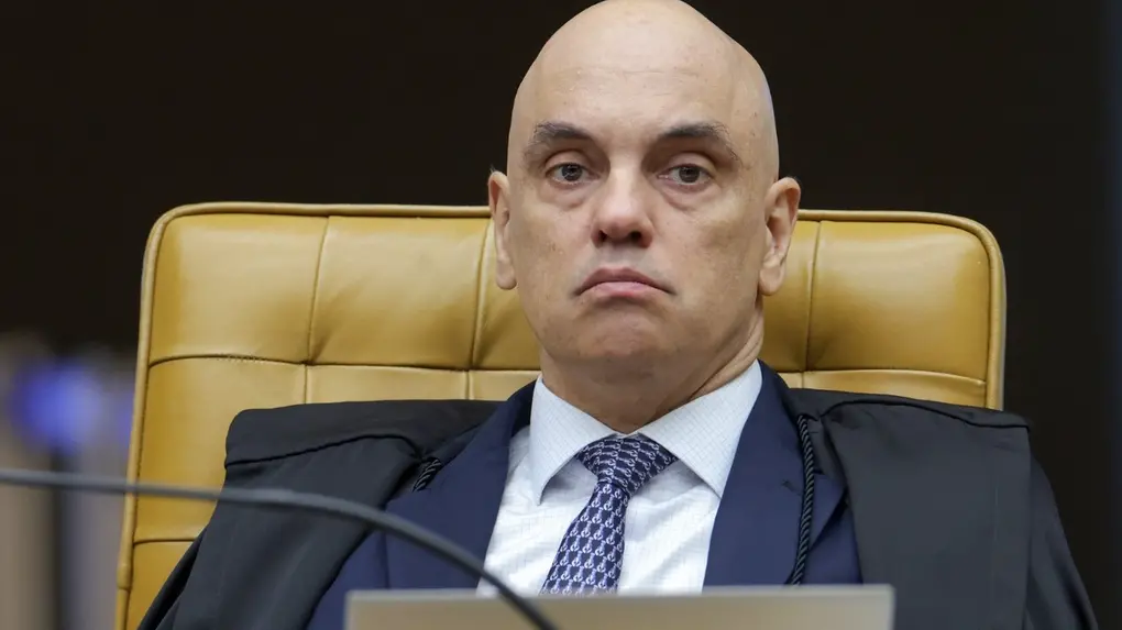 Alexandre de Moraes é um homem de meia idade, branco e careca. Na foto, ele está com expressão séria, no plenário do STF, e usa terno preto com camisa social branca e gravata estampada azul.