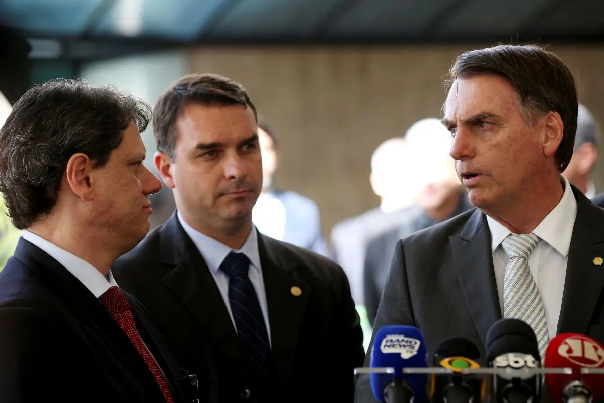 Jair Bolsonaro, Flávio Bolsonaro e Tarcísio de Freitas em uma coletiva de imprensa, com Bolsonaro no centro da fala.