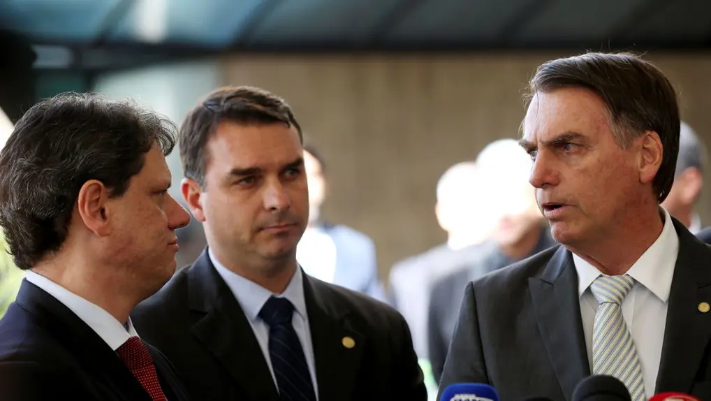 Jair Bolsonaro, Flávio Bolsonaro e Tarcísio de Freitas em uma coletiva de imprensa, com Bolsonaro no centro da fala.