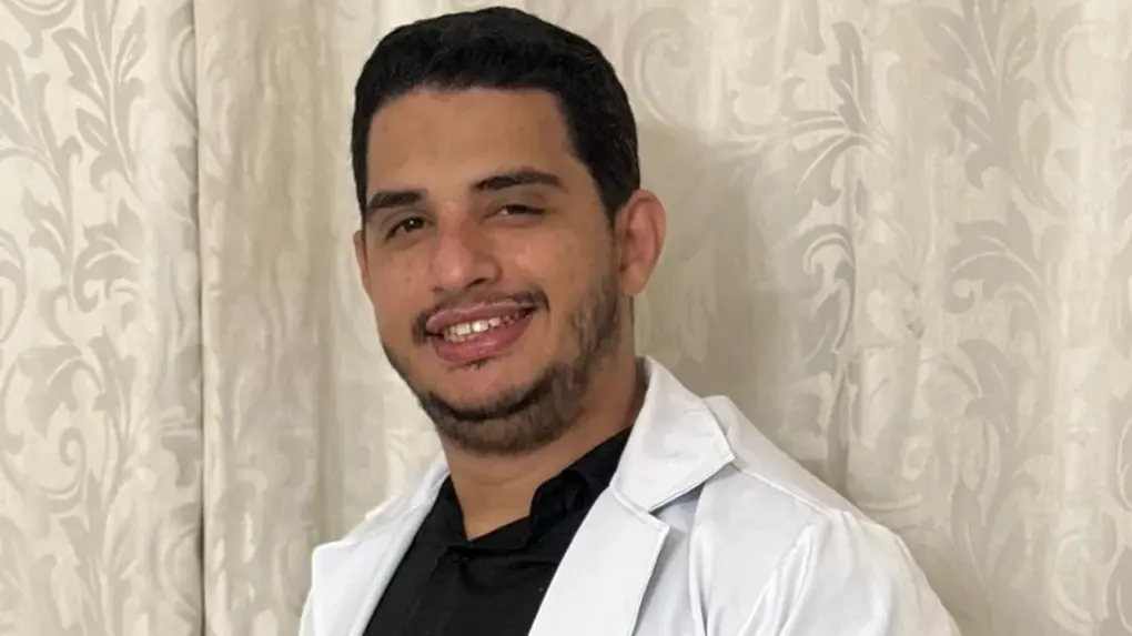 Homem com jaleco médico branco onde se lê 'Dr. Yuri Portela Médico', sorrindo para a câmera, com um emblema no braço.