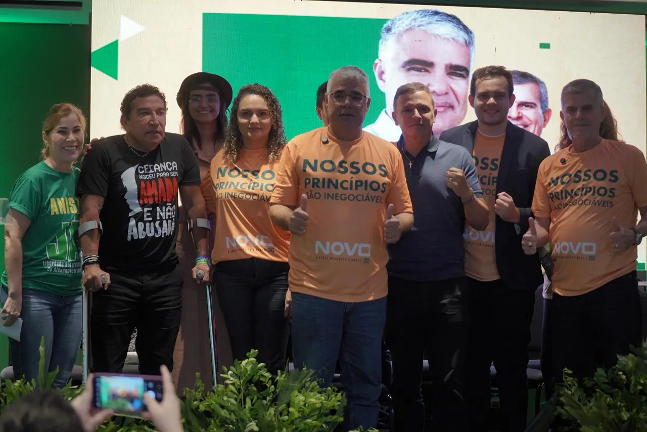 Eduardo Girão em pé, com camiseta laranja, em palanque ao lado de apoiadores.
