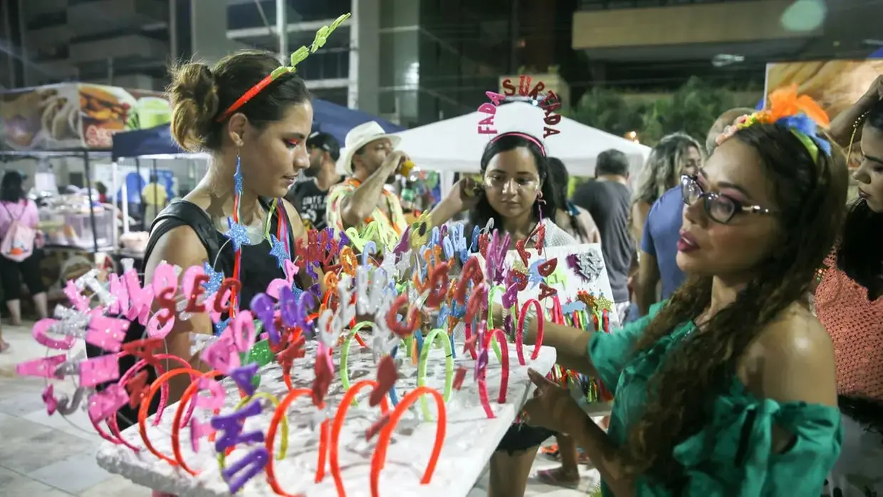 Imagem de três mulheres em barraca de venda de arquinhos de cabelo para o carnaval.
