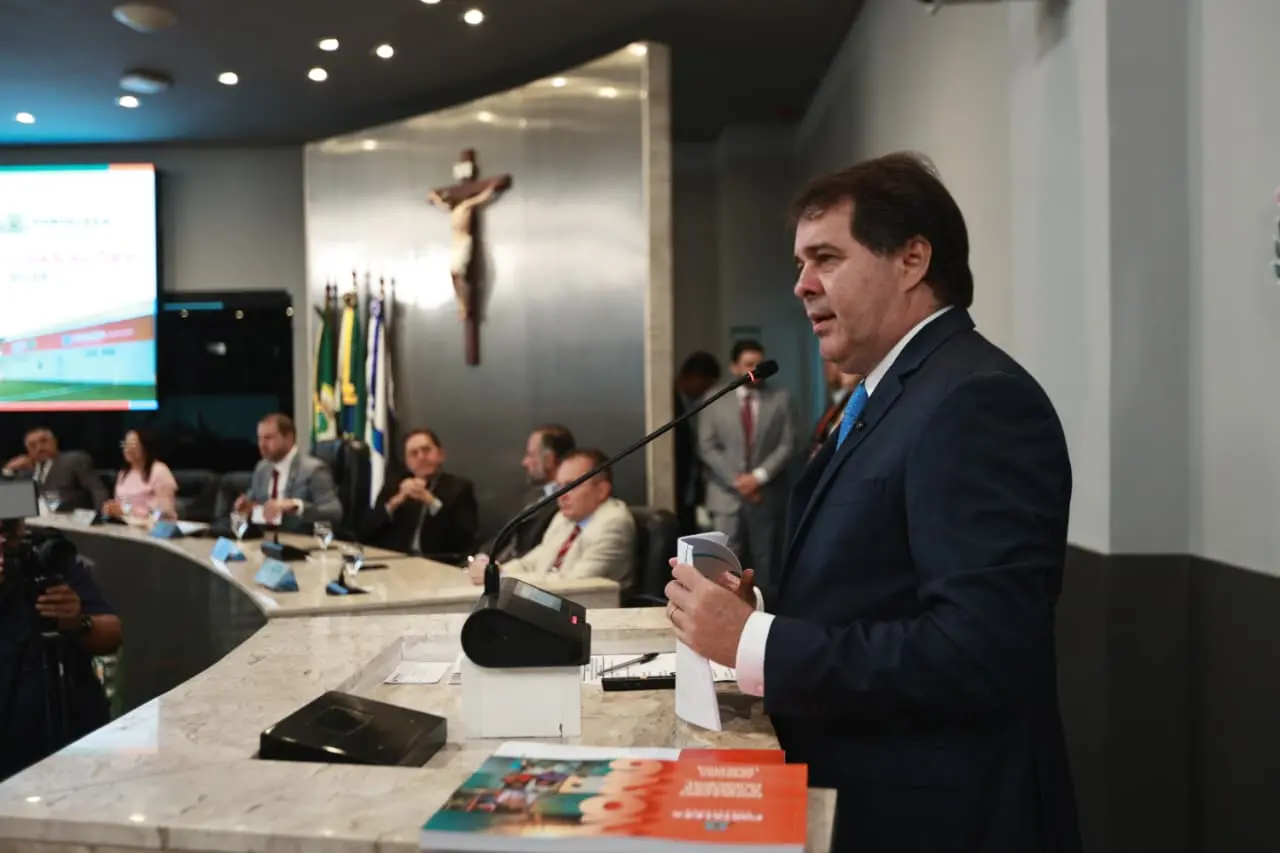 Evandro Leitão de terno escuro e gravata azul discursa em um púlpito com microfone, gesticulando com a mão direita. Ao fundo, a Mesa Diretora da Câmara de Fortaleza.
