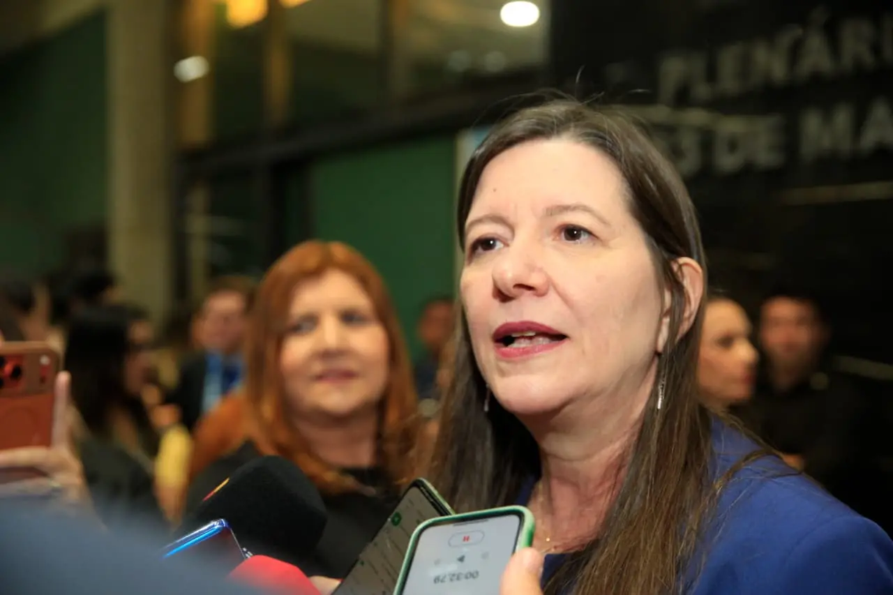 Deputada estadual licenciada Lia Gomes fala com a imprensa em ambiente interno, cercada por microfones e celulares de repórteres, durante atendimento à imprensa na Assembleia Legislativa do Ceará.