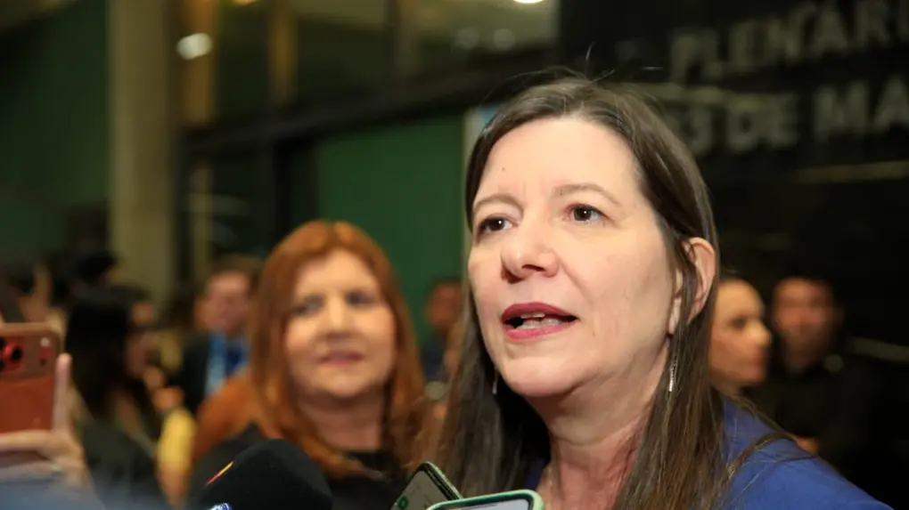 Deputada estadual licenciada Lia Gomes fala com a imprensa em ambiente interno, cercada por microfones e celulares de repórteres, durante atendimento à imprensa na Assembleia Legislativa do Ceará.