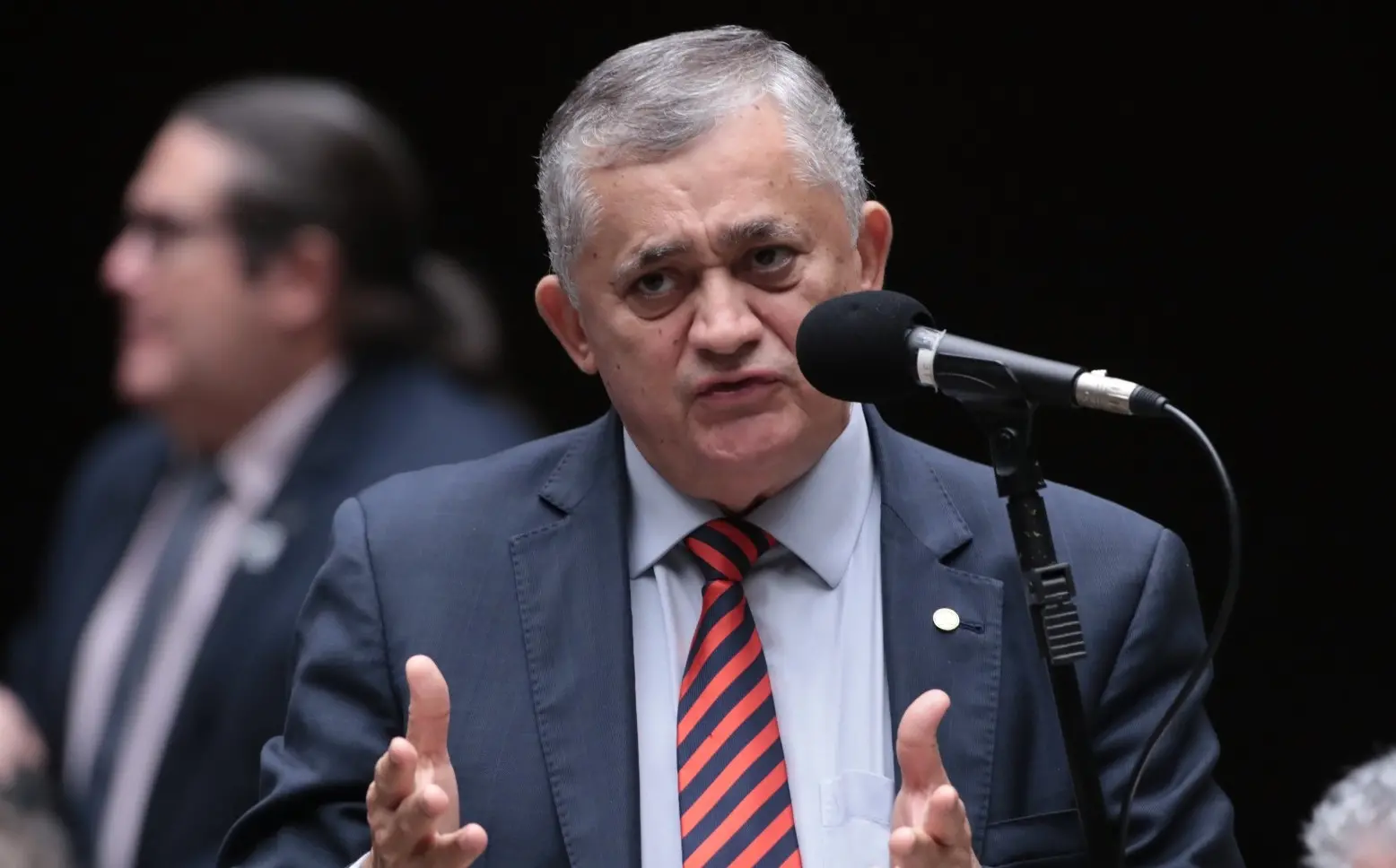 Guimarães discursa em plenário. Ele usa um terno preto com camisa social azul e gravata listrada em vermelho e preto.