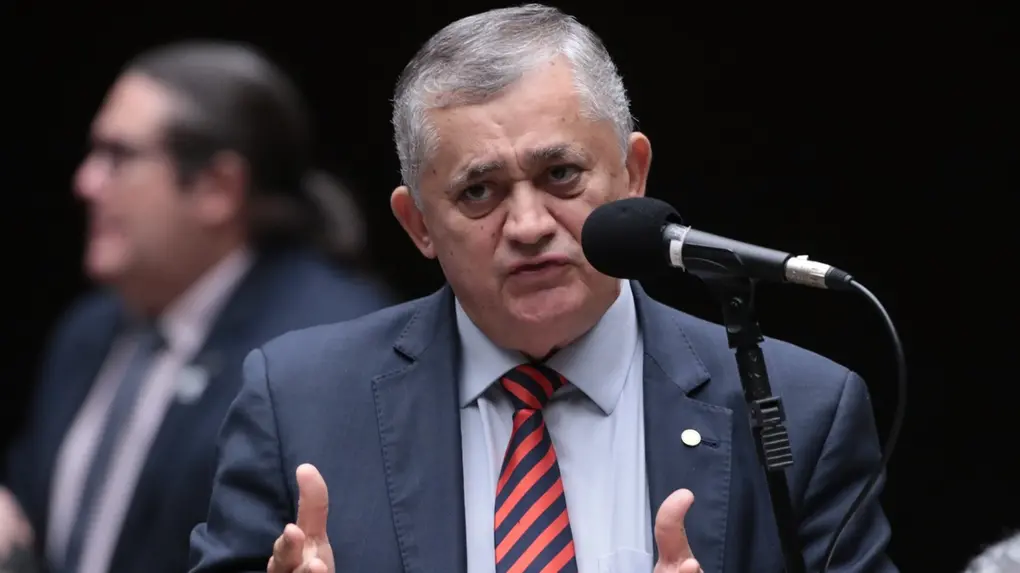 Guimarães discursa em plenário. Ele usa um terno preto com camisa social azul e gravata listrada em vermelho e preto.