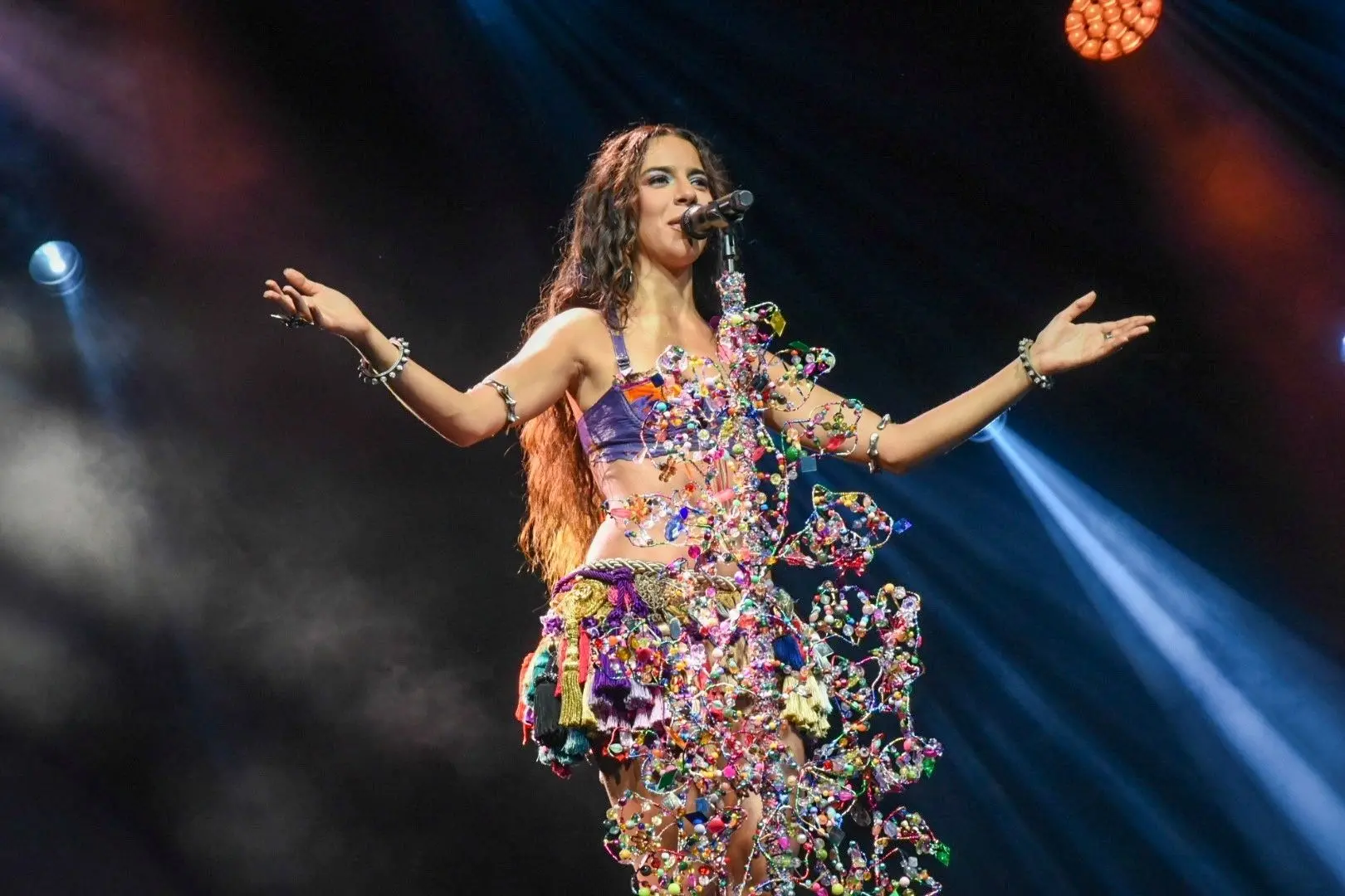 Marina Sena cantando, de braços abertos, diante de microfone.