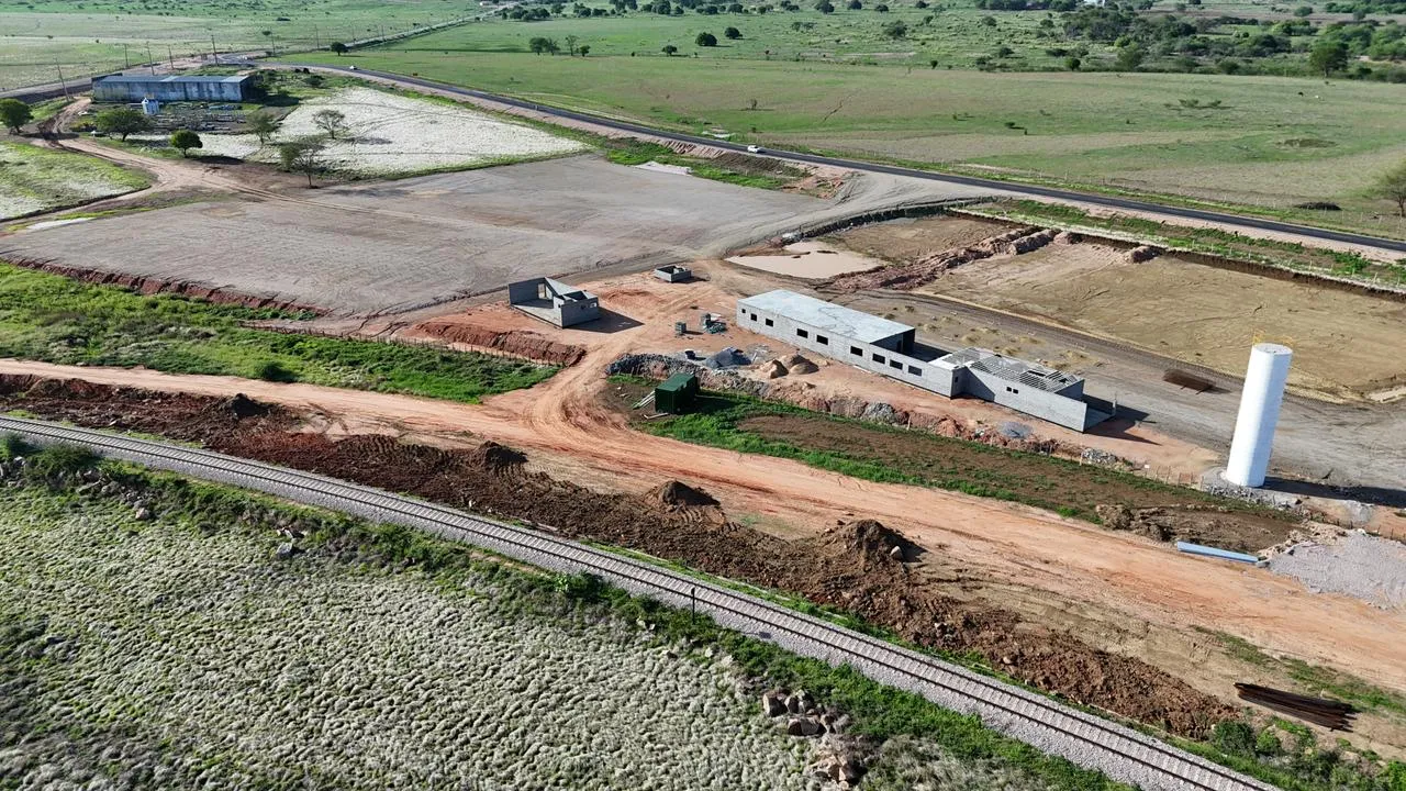 Estruturas de galpão de armazenamento, ao fundo, e o prédio administrativo sendo construído, na margem da ferrovia Transnordestina.