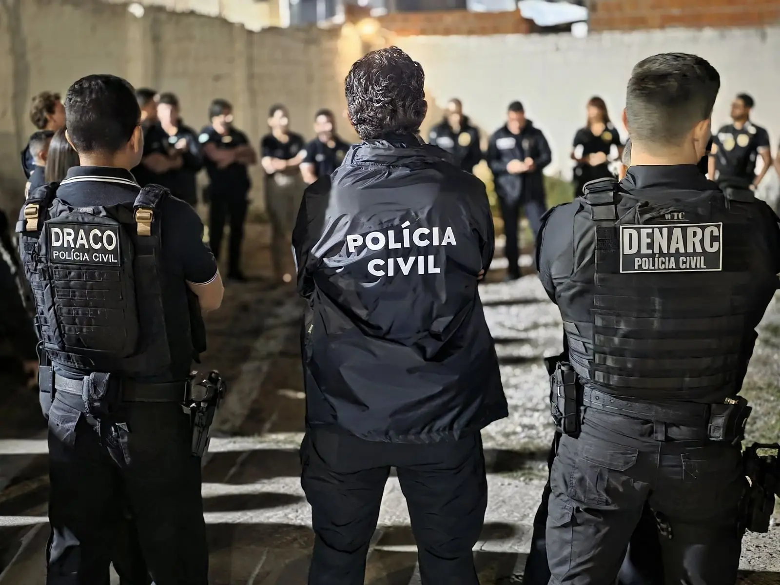 A imagem mostra vários policiais civis, em pé, fardados e armados, fazendo uma reunião antes de uma operação.