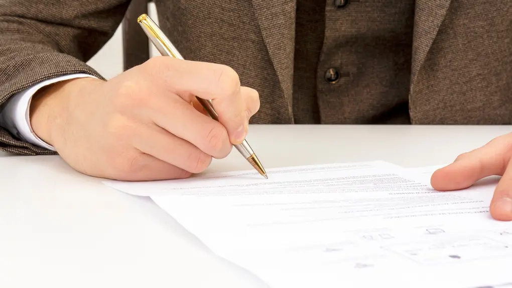 Mão de pessoa branca assinando papel.