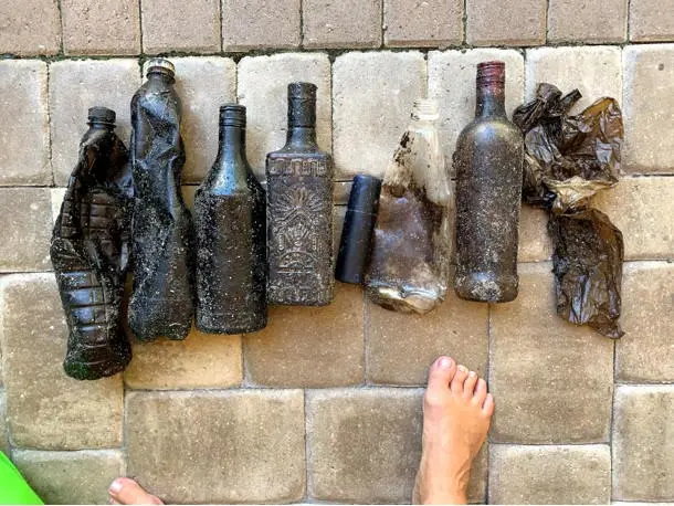 Garrafas plásticas e de vidro enfileiradas no chão, totalmente cobertas por óleo, pretas.