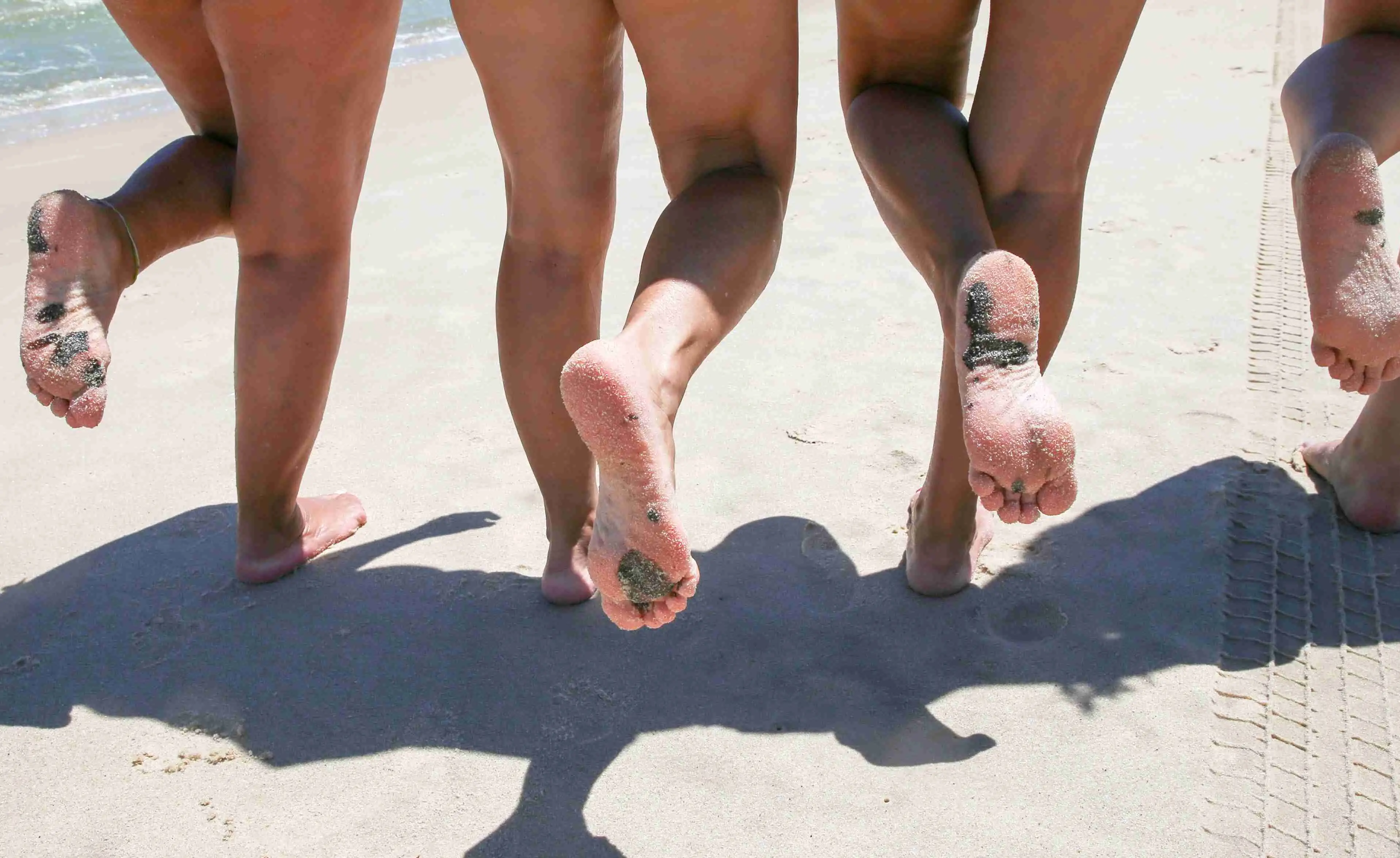 Imagem mostra pés de quatro pessoas de costas em uma praia. Os pés estão sujos de manchas de óleo.