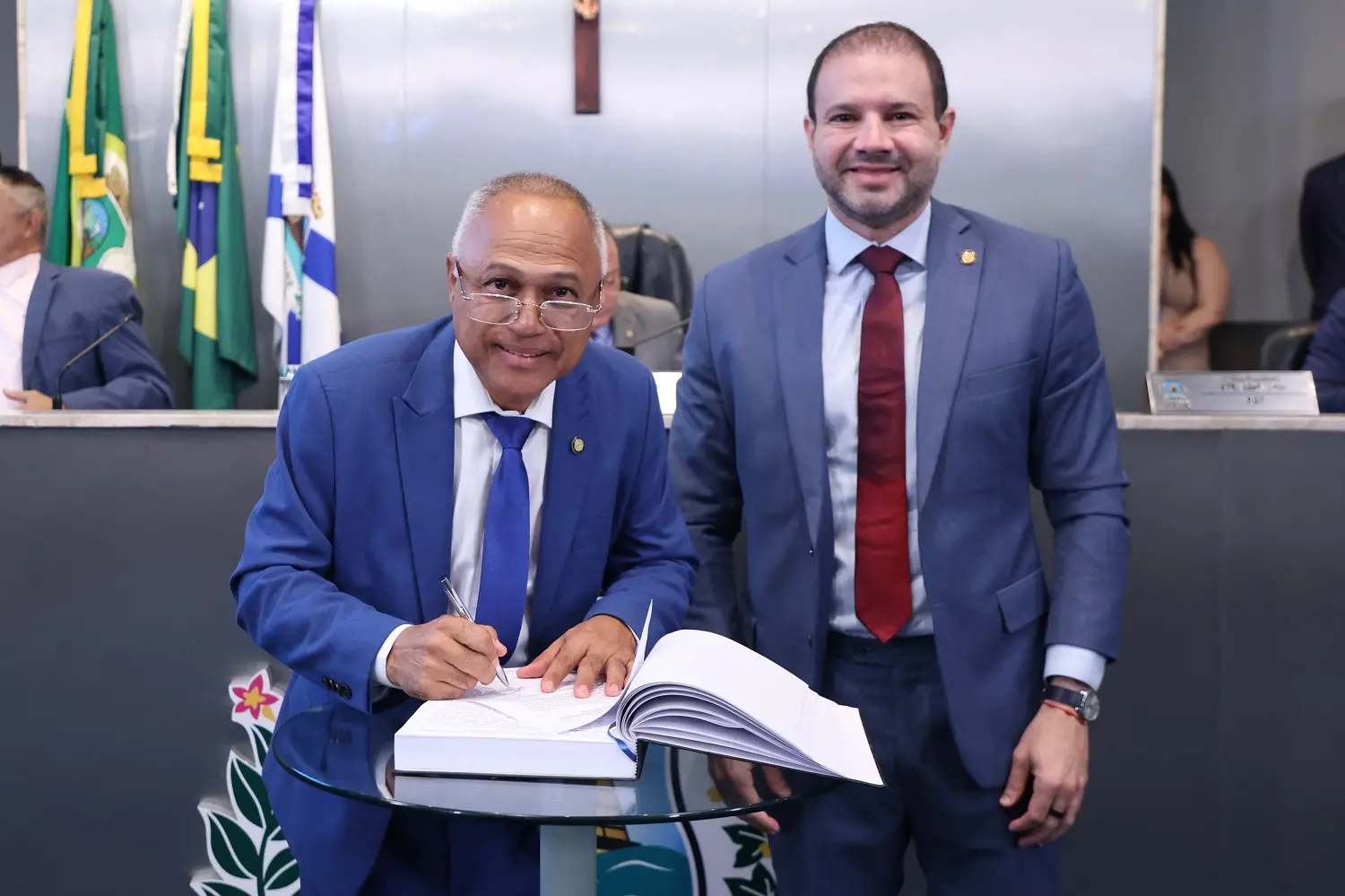 Cônsul do Povo e Leo Couto, lado a lado, enquanto o parlamentar assina o termo de posse.