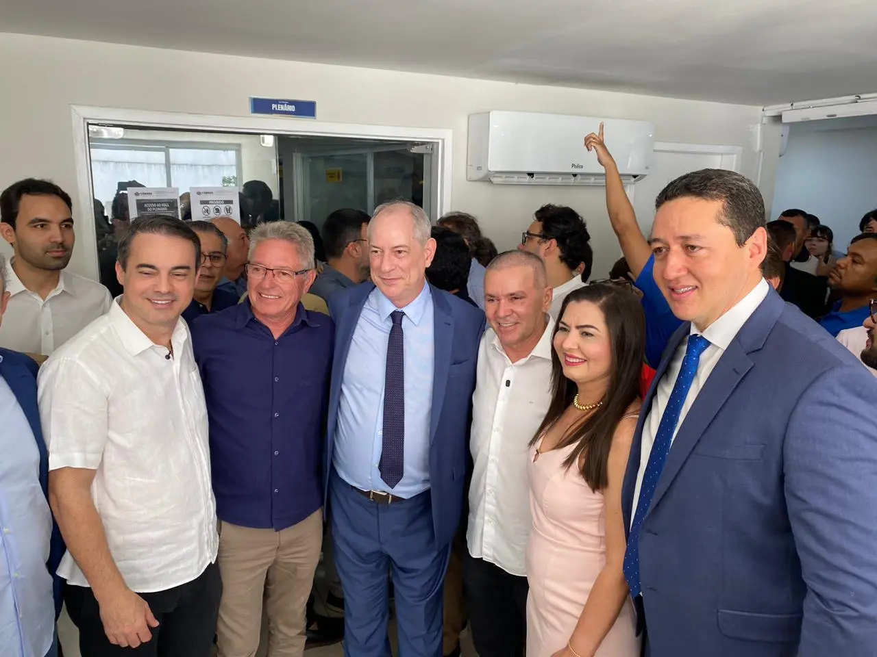 Ciro Gomes posa ao lado de Capitão Wagner, Alcides Fernandes e Glêdson Bezerra em frente à entrada de um plenário. O grupo sorri para a foto em um ambiente interno movimentado, com Ciro em destaque vestindo terno azul.