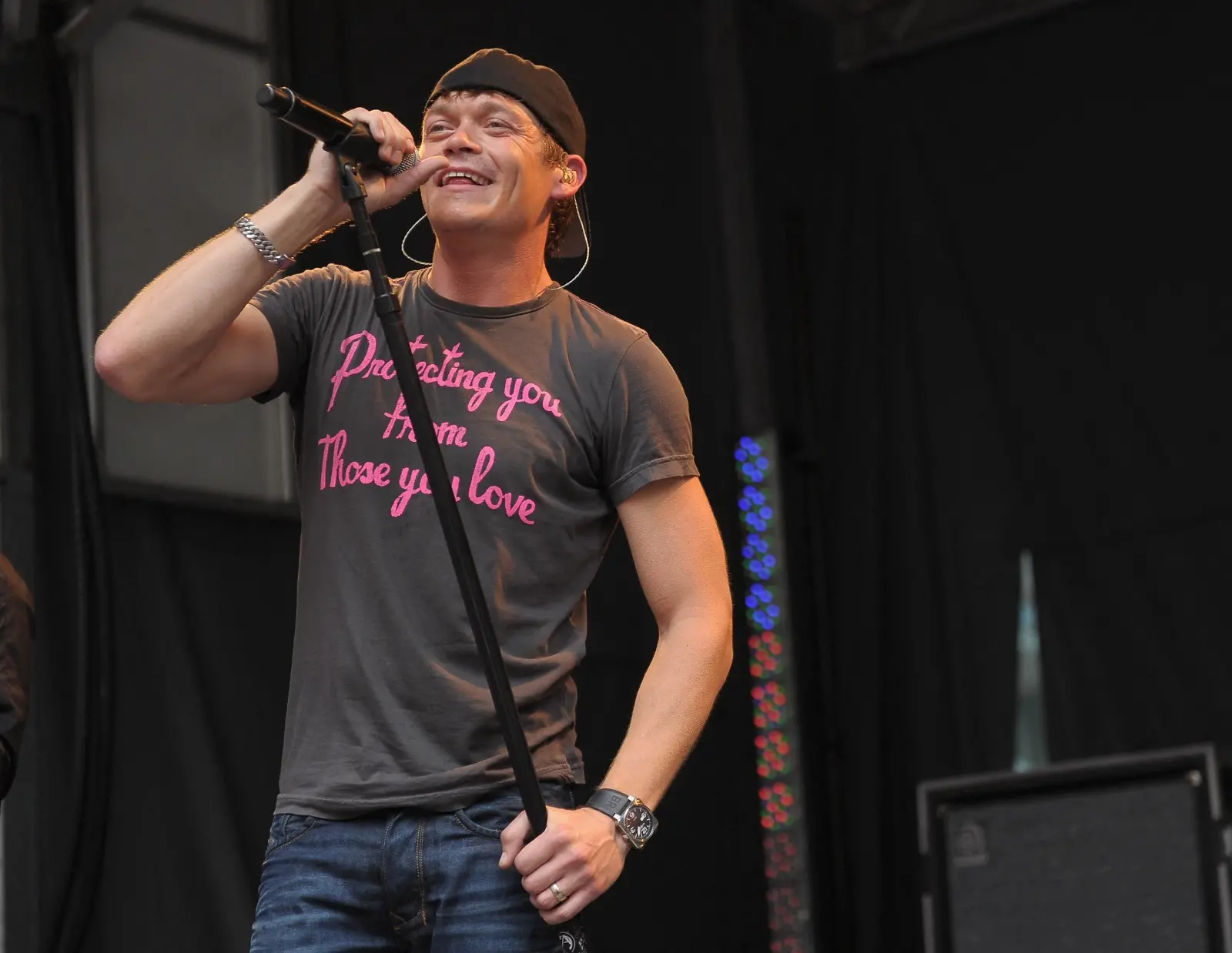 Imagem mostra o vocalista da banda 3 Doors Down puxando um microfone com pedestal para cantar em show.