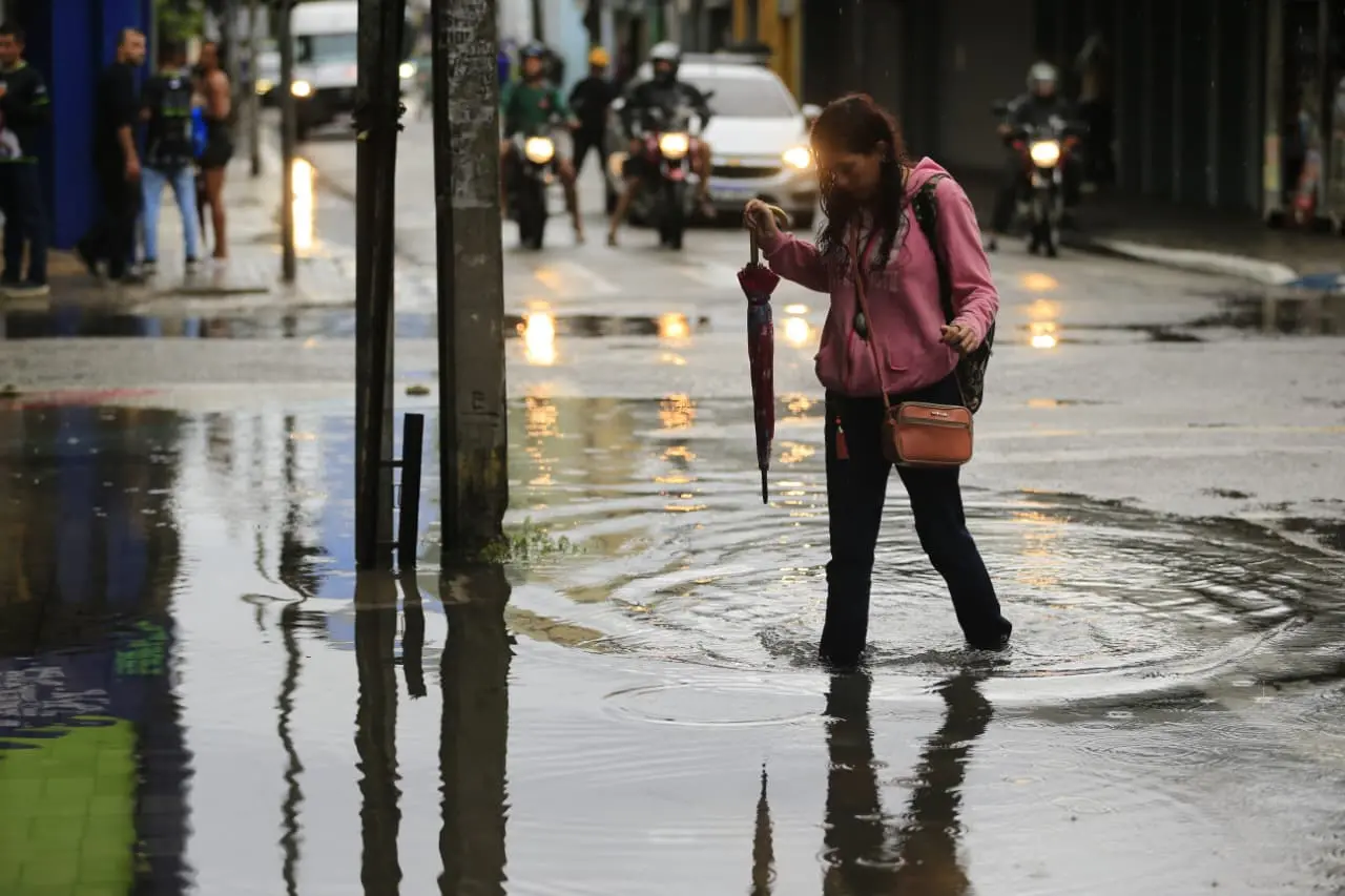 Mulher segura guarda-chuva fechado enquanto caminha por grande poça de água.