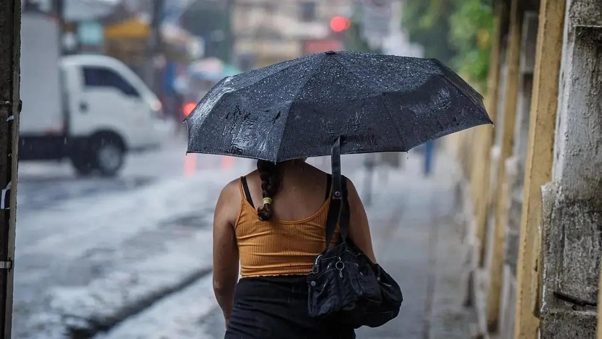 mulher de costas segurando guarda-chuva chovendo.