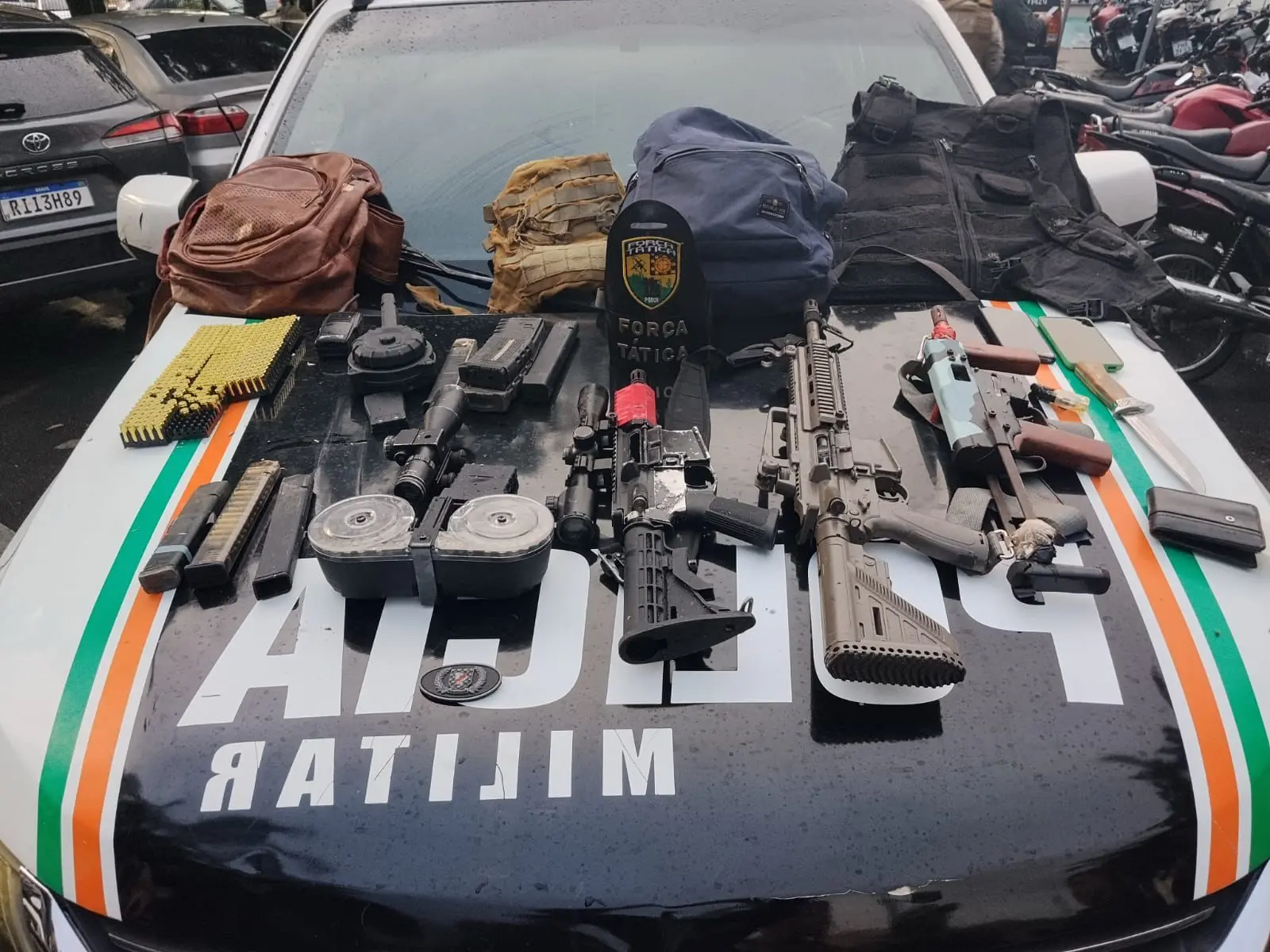 Armamento apreendido pela polícia em operação que inclui pistolas, escopeta, munições e equipamentos táticos, exibidos sobre o veículo policial com a logomarca da Polícia Militar no Ceará.