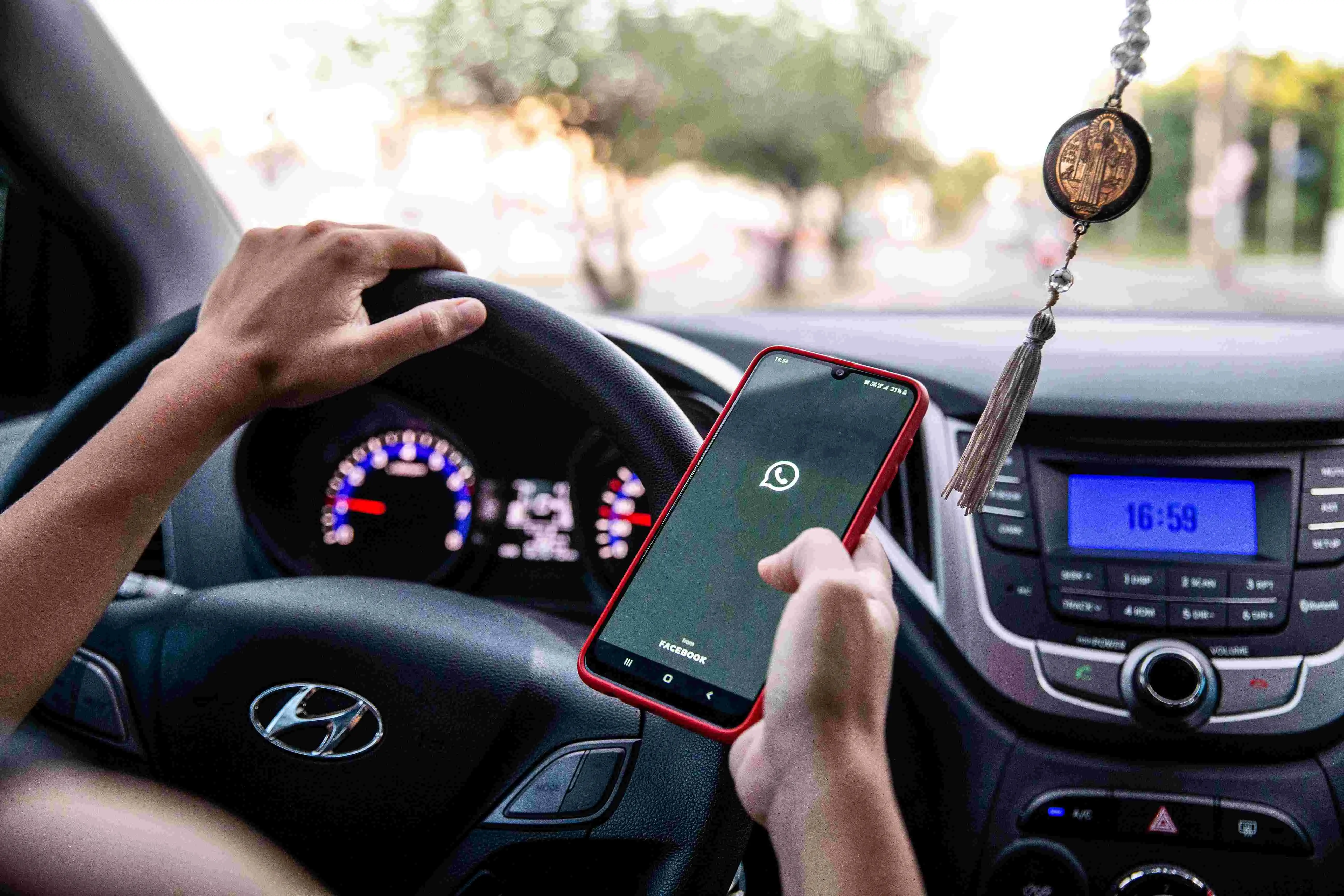 Uma pessoa com uma mão no volante de um carro Hyundai e a outra segurando um celular com o aplicativo WhatsApp aberto.