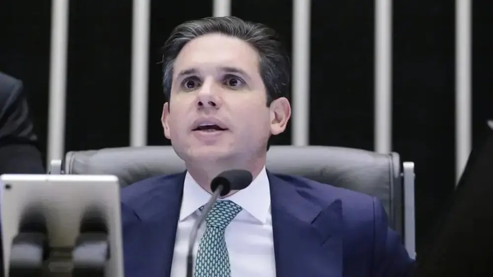 Homem de terno e gravata verde falando em microfone em um plenário. Imagem usada em matéria onde Hugo Motta envia PEC do fim da escala 6x1 à CCJ.