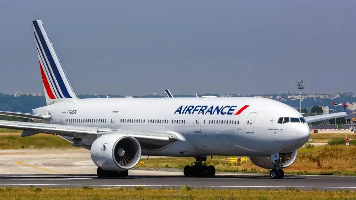 Aeronave da Air France, modelo Boeing 777-300ER, taxiando em uma pista de aeroporto sob luz solar clara. O avião é branco com o logotipo 