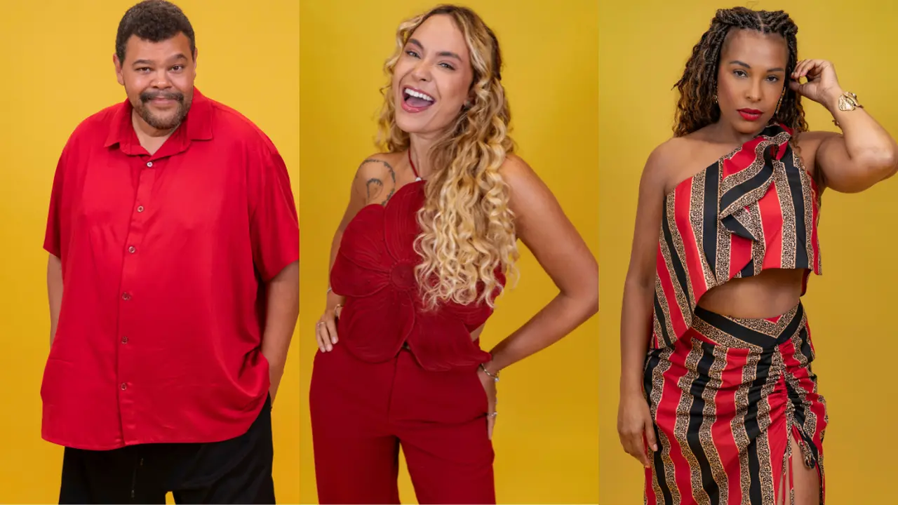 Três pessoas, um homem e duas mulheres, posam sorrindo contra um fundo amarelo vibrante. O homem é Babu, e veste uma camisa vermelha. A mulher do meio é Sarah Andrade, que usa um conjunto vermelho com top em formato de flor, e a mulher da direita, é Sol Vega, que veste um conjunto listrado vermelho e preto. Eles são participantes do BBB 26 e estão no paredão.
