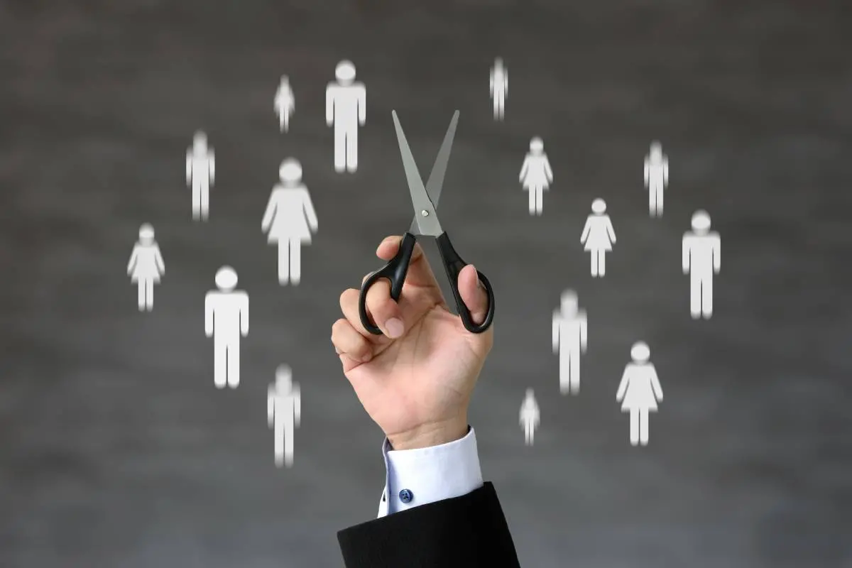 Imagem mostra uma mão de um homem branco segurando uma tesoura. Ao fundo, ilustração representativa de pessoas.