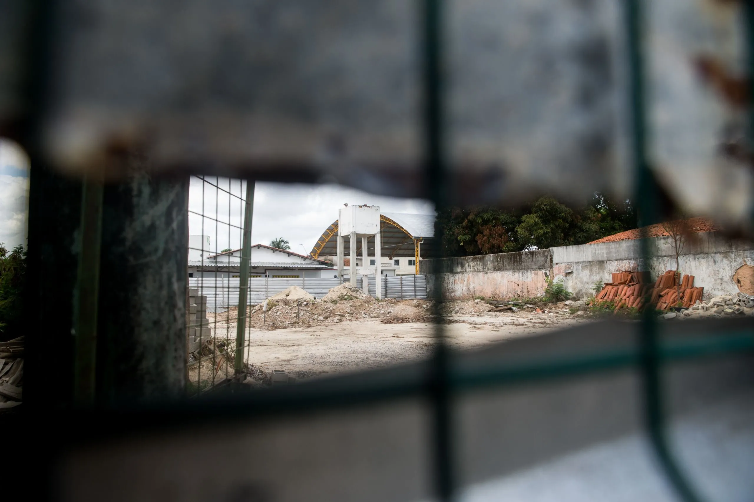 Materiais de construção e entulho podem ser visto através dos tapumes que isolam a escola.