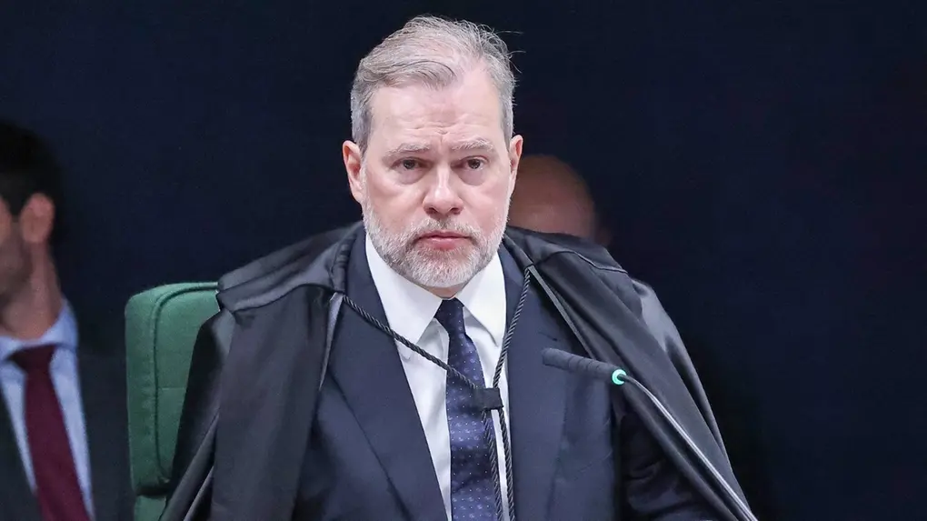 Dias Toffoli é um homem branco de cabelo liso ralo grisalho e barba bem cortada da mesma cor. Na foto, ele está com semblante sério e veste terno preto com camisa social branca e gravata azul.