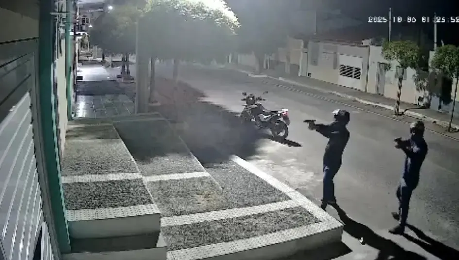 Foto de câmera de segurança noturna mostrando dois policiais armados com pistolas, um deles com capacete, em uma rua escura com uma motocicleta estacionada ao fundo. Imagem usada em matéria sobre atentado contra vereadora do Rio Grande do Norte.