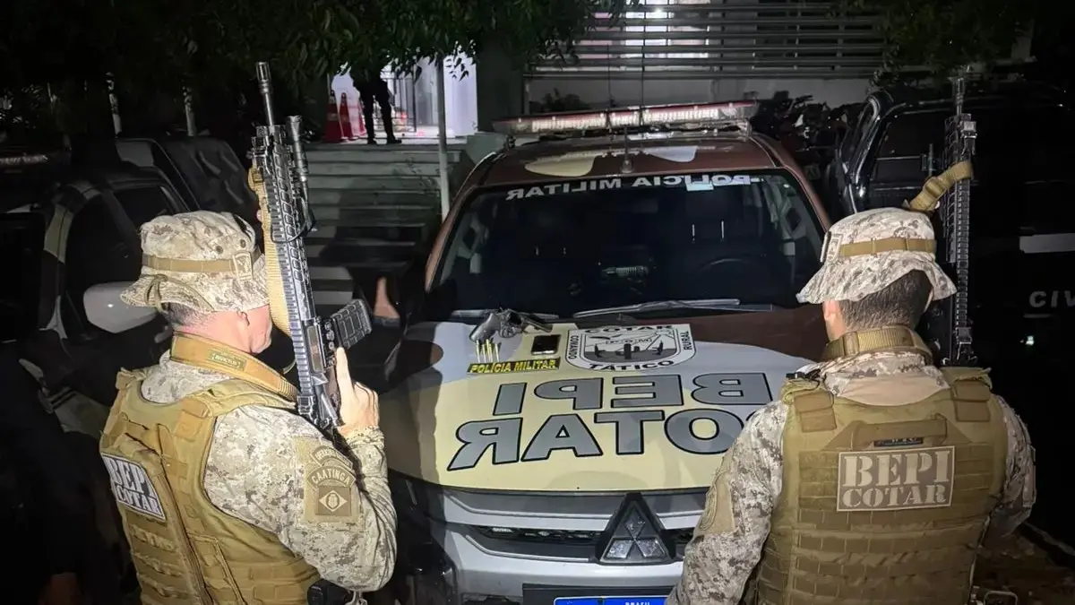 Policiais do BEPI COTAR, em uniforme camuflado e armados, posicionados ao lado de viatura da Polícia Militar durante operação noturna.