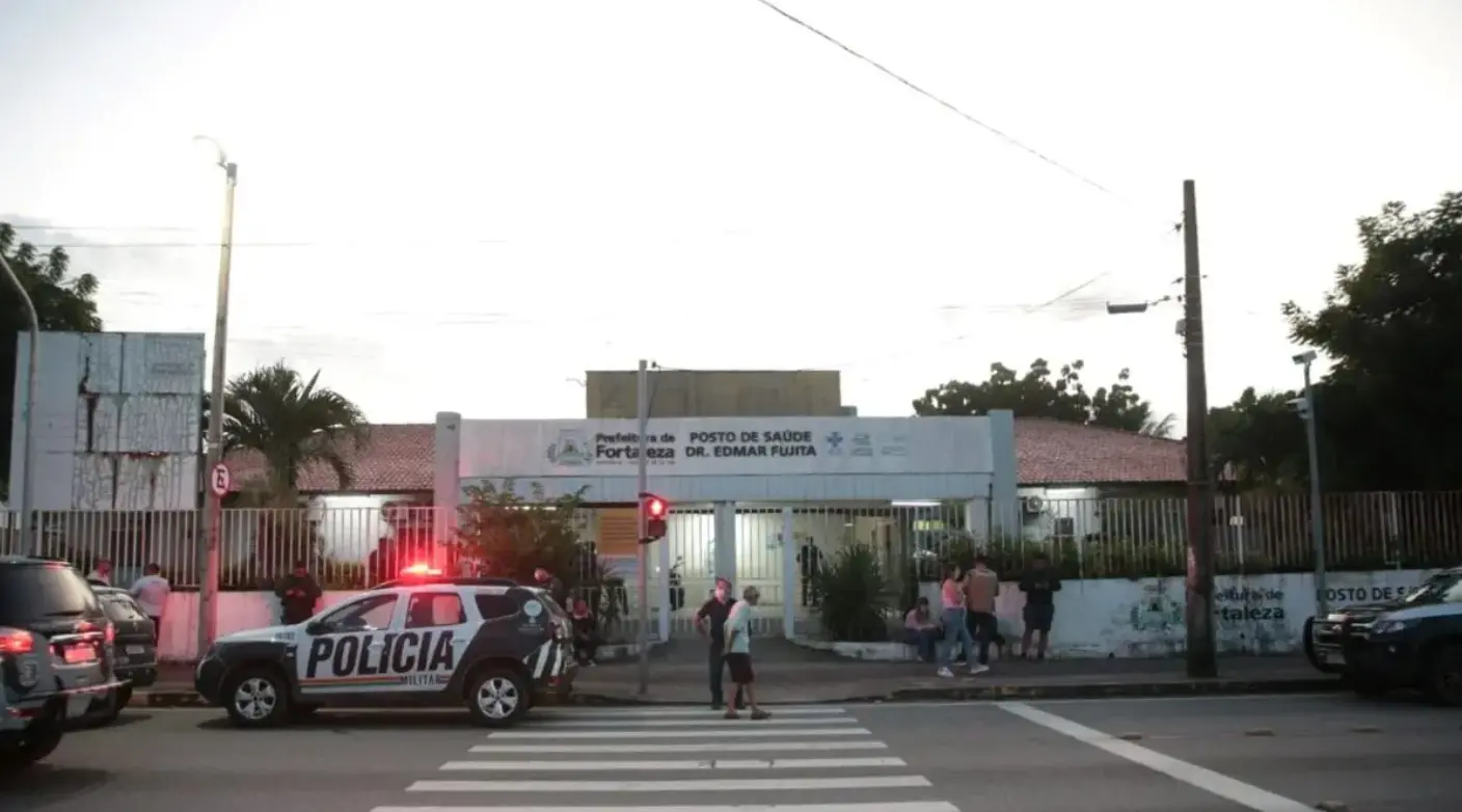 Imagem da fachada do posto de saúde Edmar Fujita com movimentação intensa no local e presença de viaturas da PM.