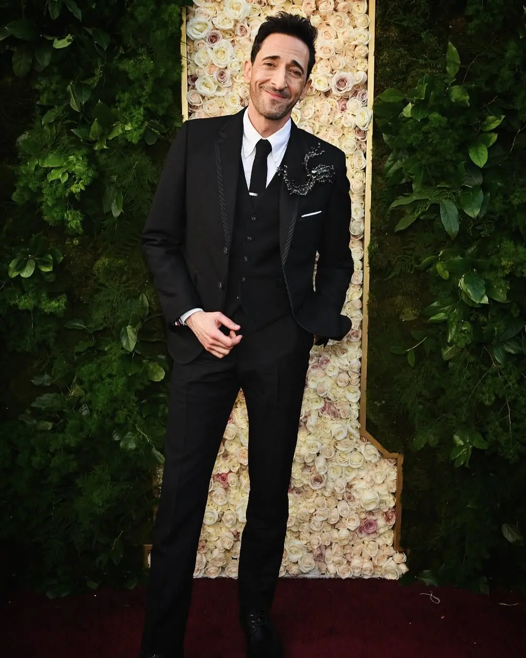 Imagem do ator posando para foto. Ele veste um terno preto.