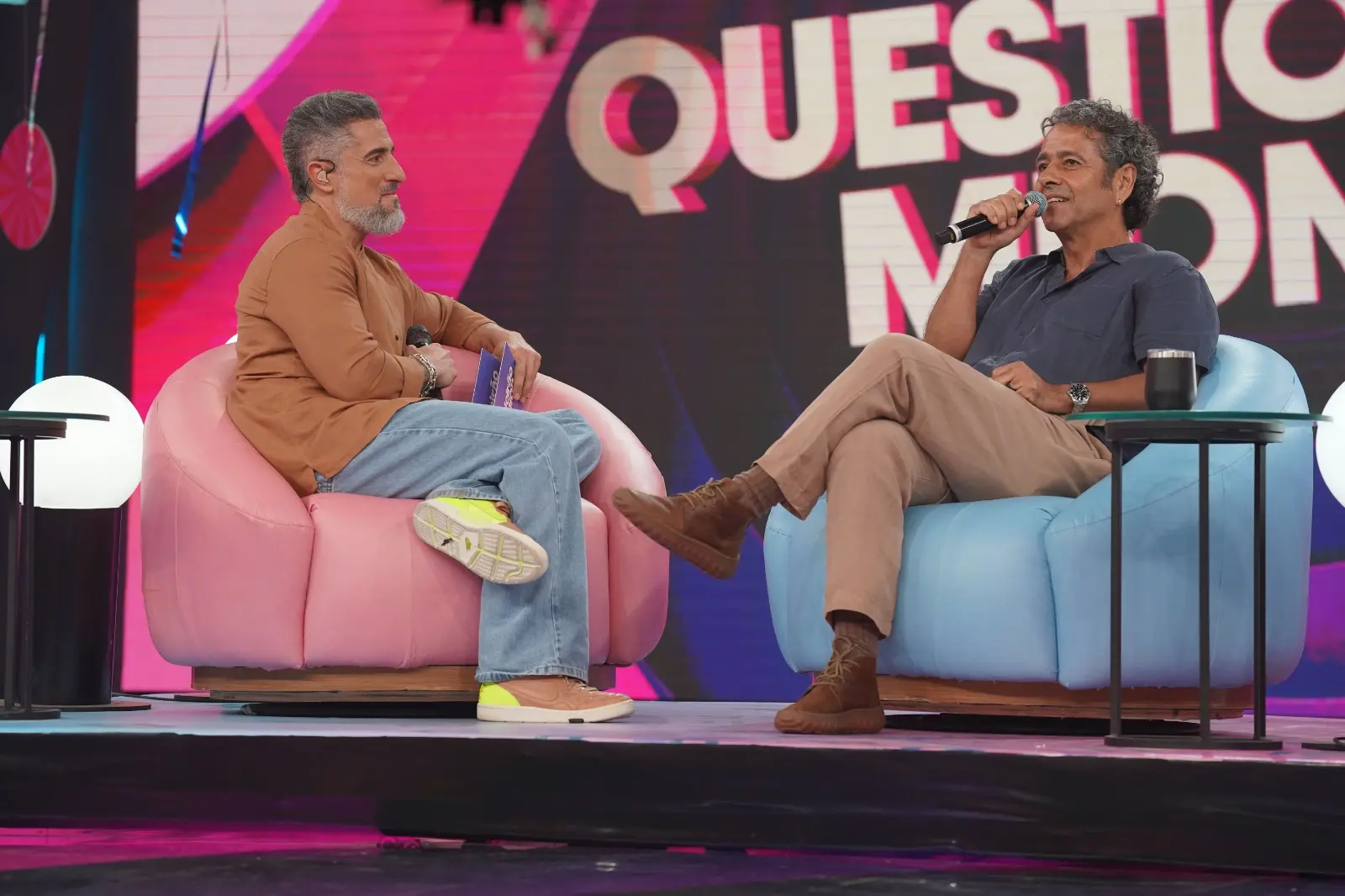 Marcos Mion e Marcos Palmeira sentados conversando.