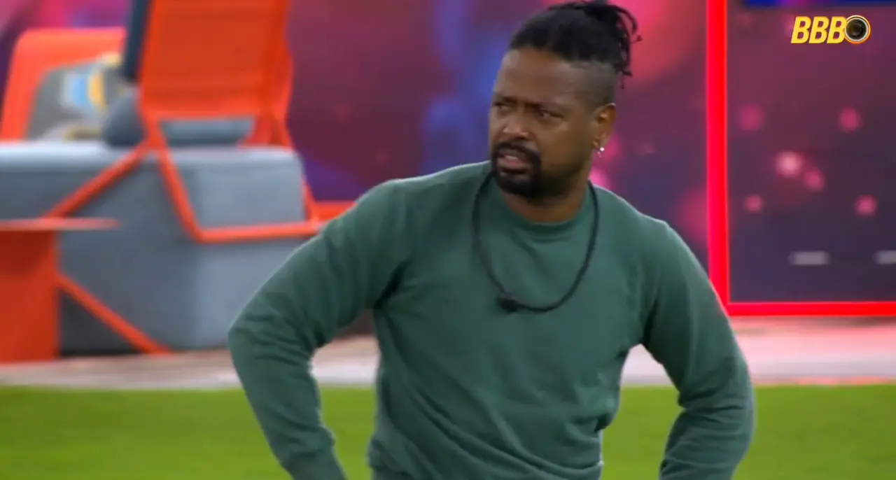 Leandro Boneco, homem negro de cabelo preto amarrado, barba e bigode pretos, com blusa de manga longa verde.