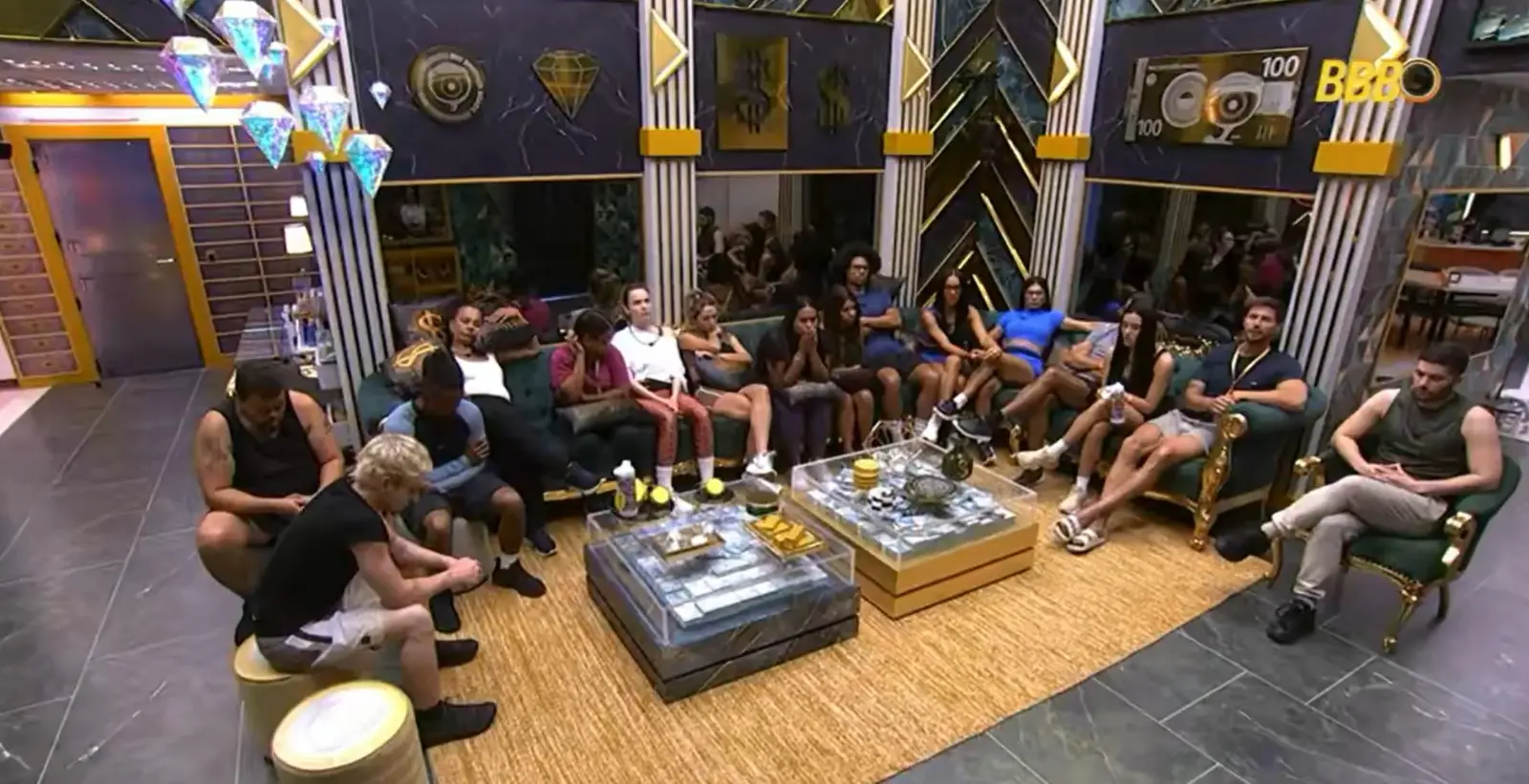 Imagem de um grupo de participantes do Big Brother Brasil sentados em uma sala decorada, assistindo a uma atividade ou conversa, com ambiente moderno e luxuoso.